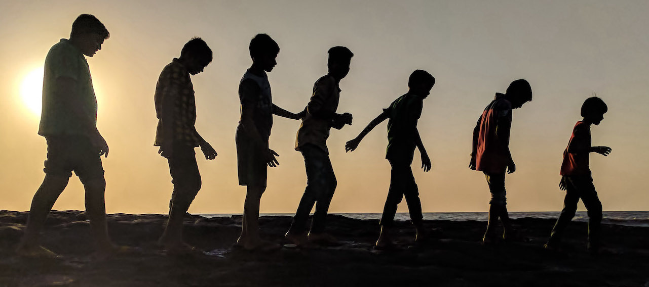 Kids silhouette walking in a line by the water