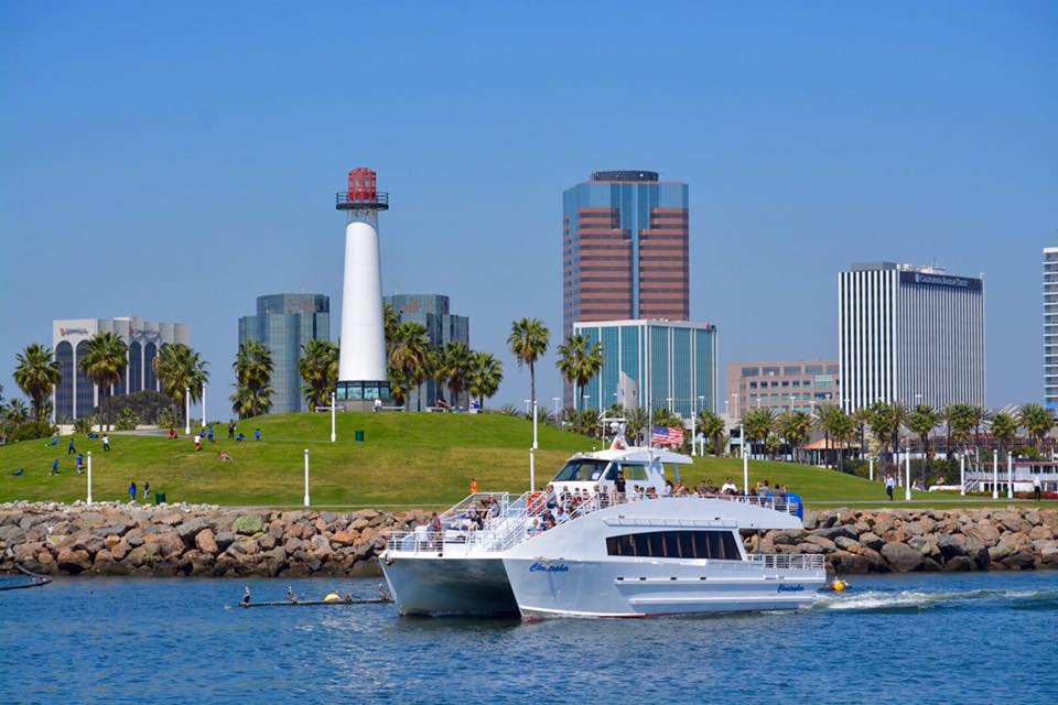 A scenic view of a tour boat on the water in Long Beach overlooking buildings downtown